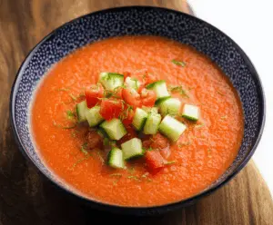 Fresh and vibrant gazpacho soup in a bowl, garnished with chopped vegetables and herbs, served outdoors on a sunny day.